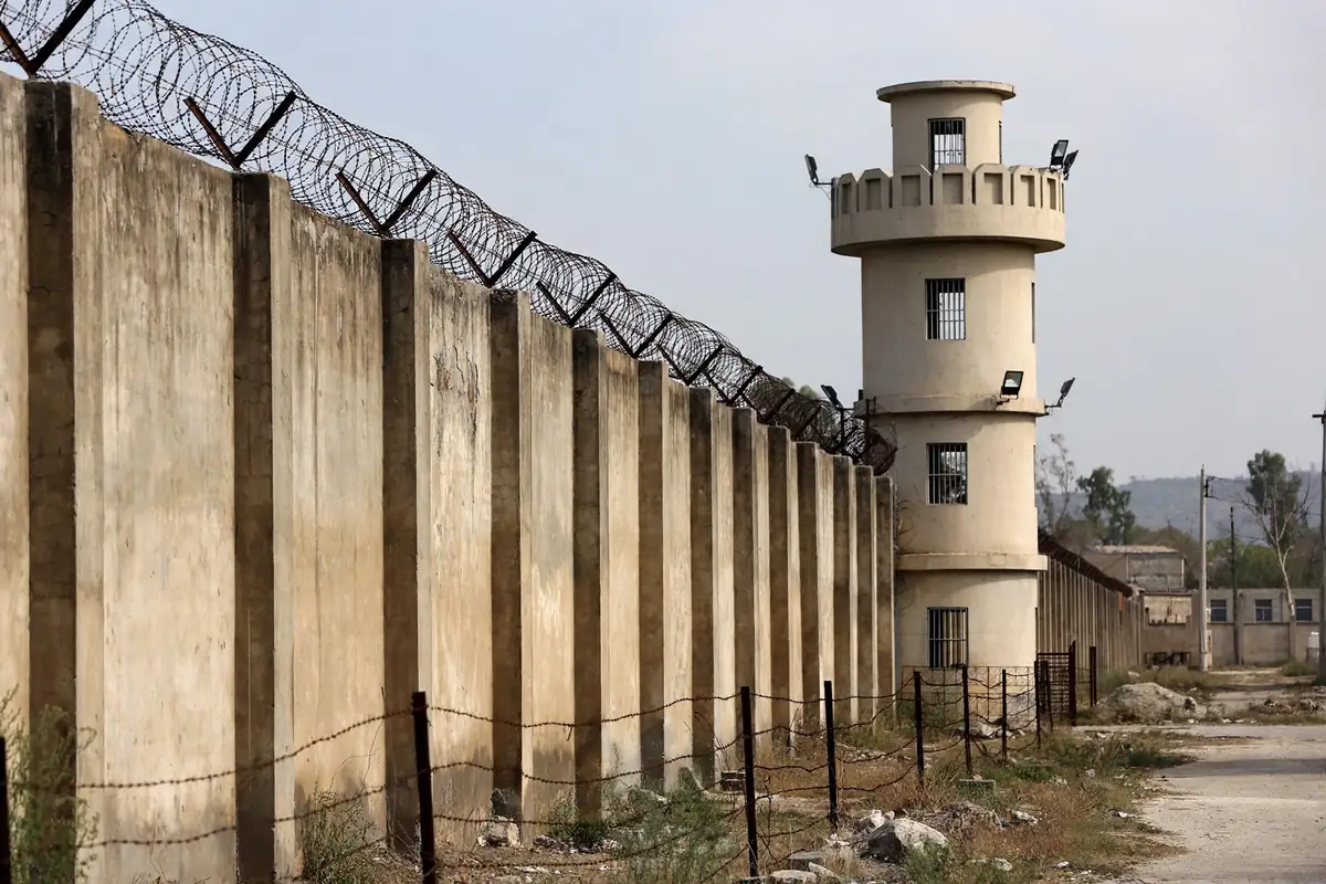 High prison perimeter wall topped with barbed wire and a watchtower