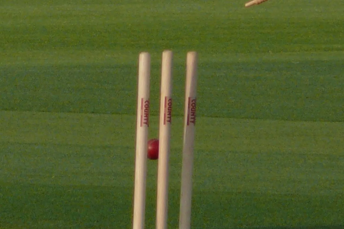 A cricket ball hitting the stumps with the bails flying