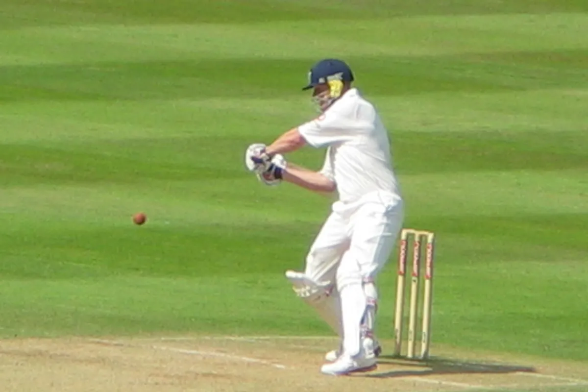 A batter hits a six during a cricket match on a green outfield