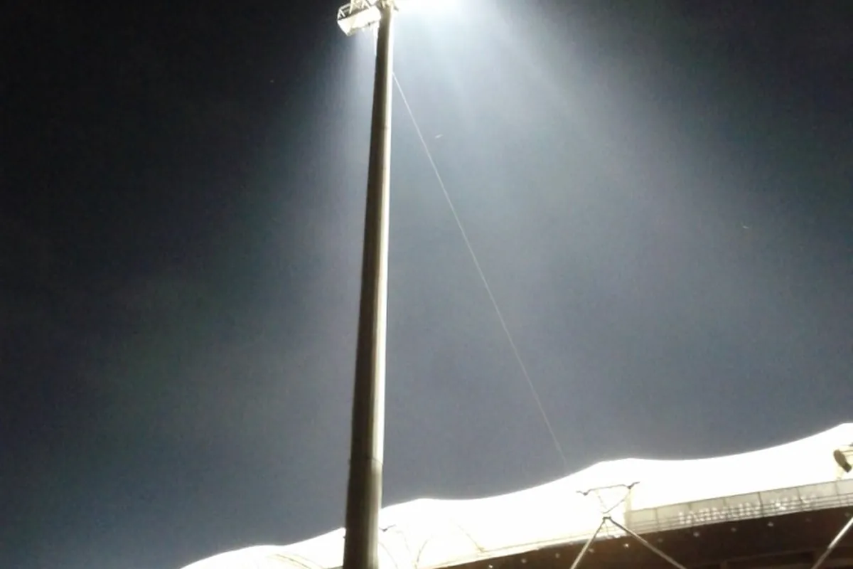 A floodlight mast shining over a cricket stadium at night